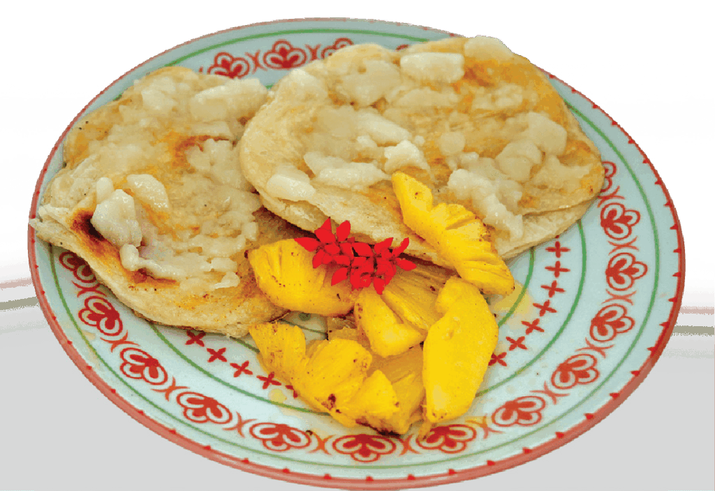 Thin pancakes or crepes are served with fruit and a red flower garnish on a patterned plate.