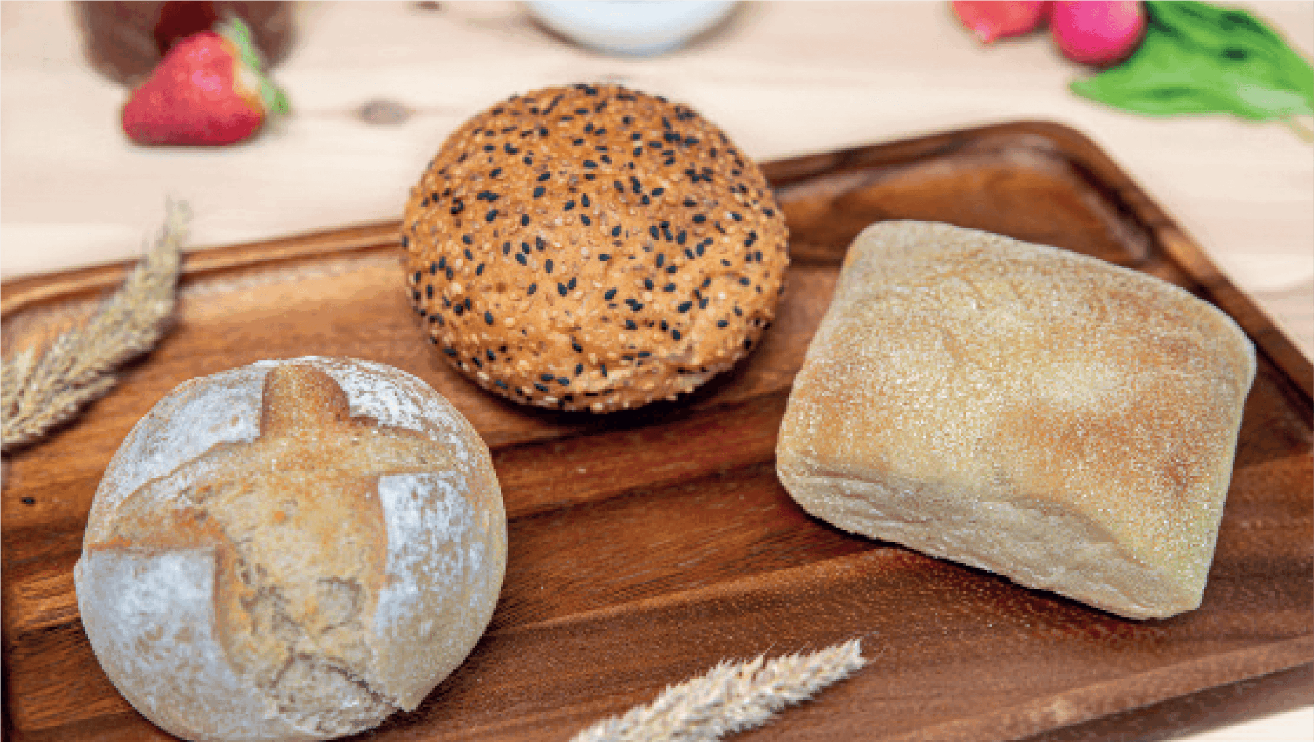Three assorted bread rolls – a kaiser roll, a sesame seed bun, and a ciabatta – are displayed on a wooden tray.
