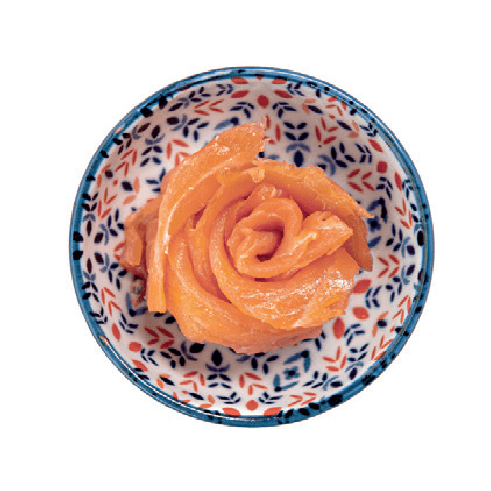 Thin slices of smoked salmon are artfully arranged in a rose shape within a small patterned bowl.
