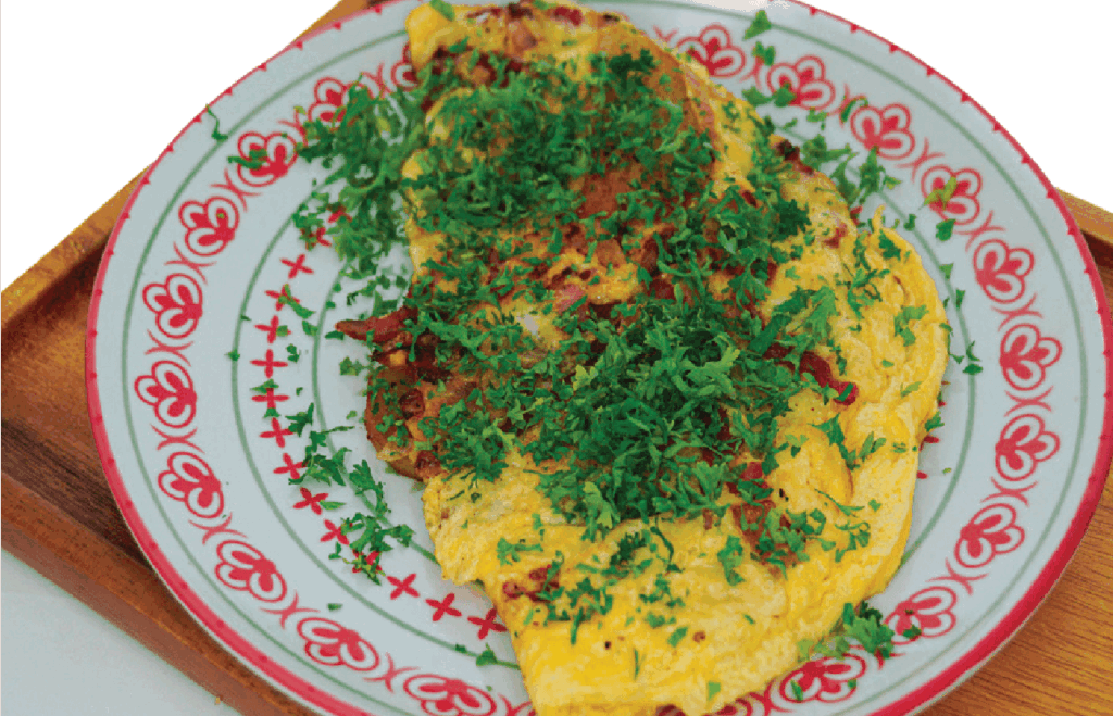 A folded omelette, possibly with bacon, is generously topped with fresh chopped parsley on a patterned plate.