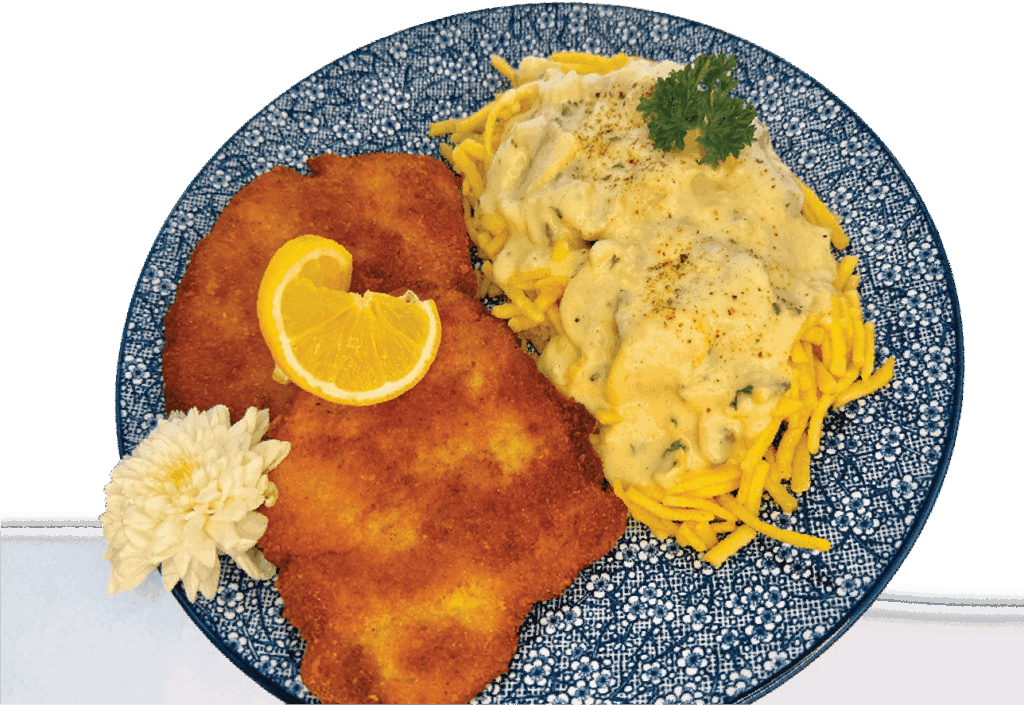 Two breaded schnitzels are served with creamy cheese spaetzle (Käsespätzle), a lemon wedge, and a flower garnish.