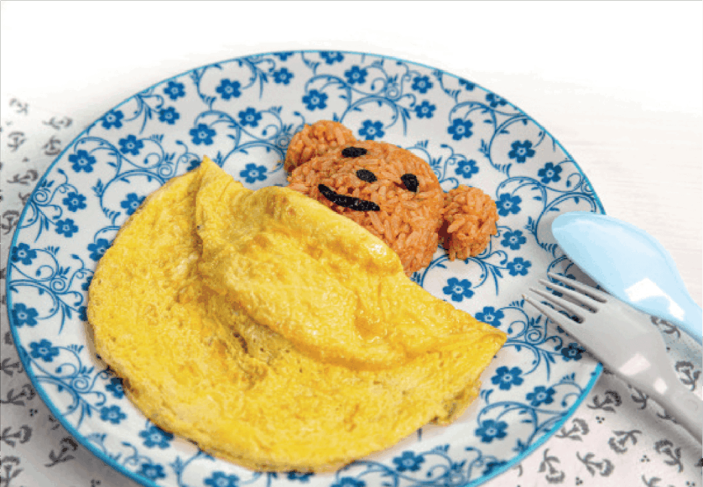 An omelette is served beside rice shaped like a teddy bear's head on a blue floral plate.