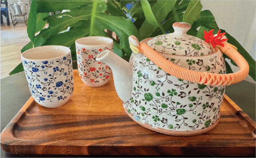 A floral patterned teapot with a wrapped handle and two matching cups are set on a wooden tray.