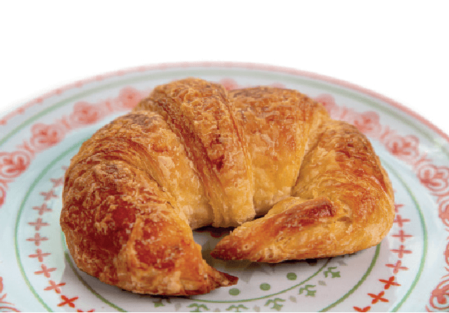 A flaky, golden-brown croissant is presented on a plate with a red and green patterned rim.