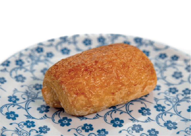 A golden-brown pain au chocolat sits on a decorative blue and white floral plate.