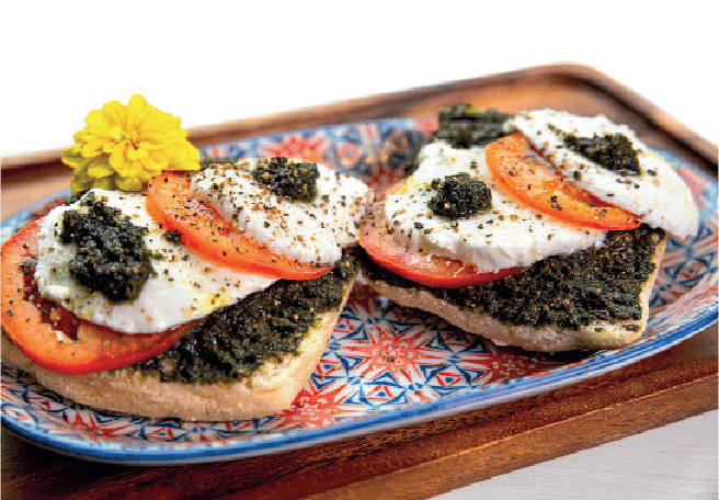 Two open-faced sandwiches with pesto, mozzarella, and tomato slices are arranged on a colorful patterned plate.