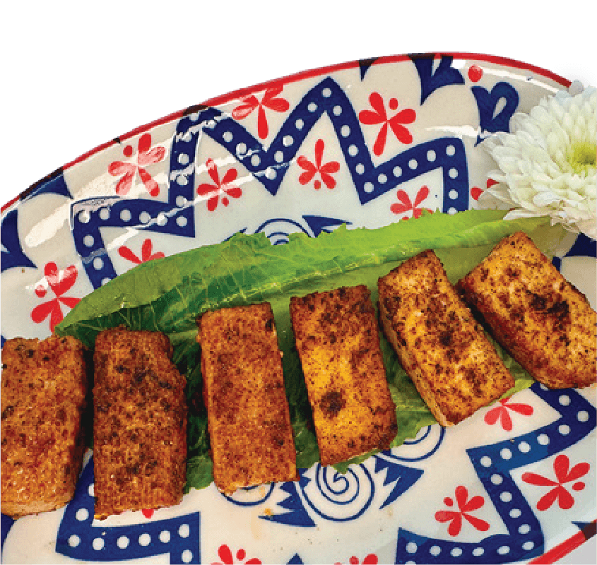 Six rectangular, seasoned pieces of fried tofu are arranged on a lettuce leaf on a red, white, and blue patterned plate with a white flower garnish.
