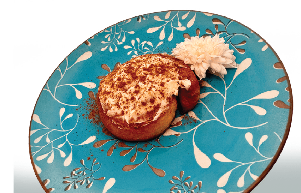 A fluffy cinnamon roll topped with cream cheese frosting and a sprinkle of cinnamon sits on a decorative blue plate.